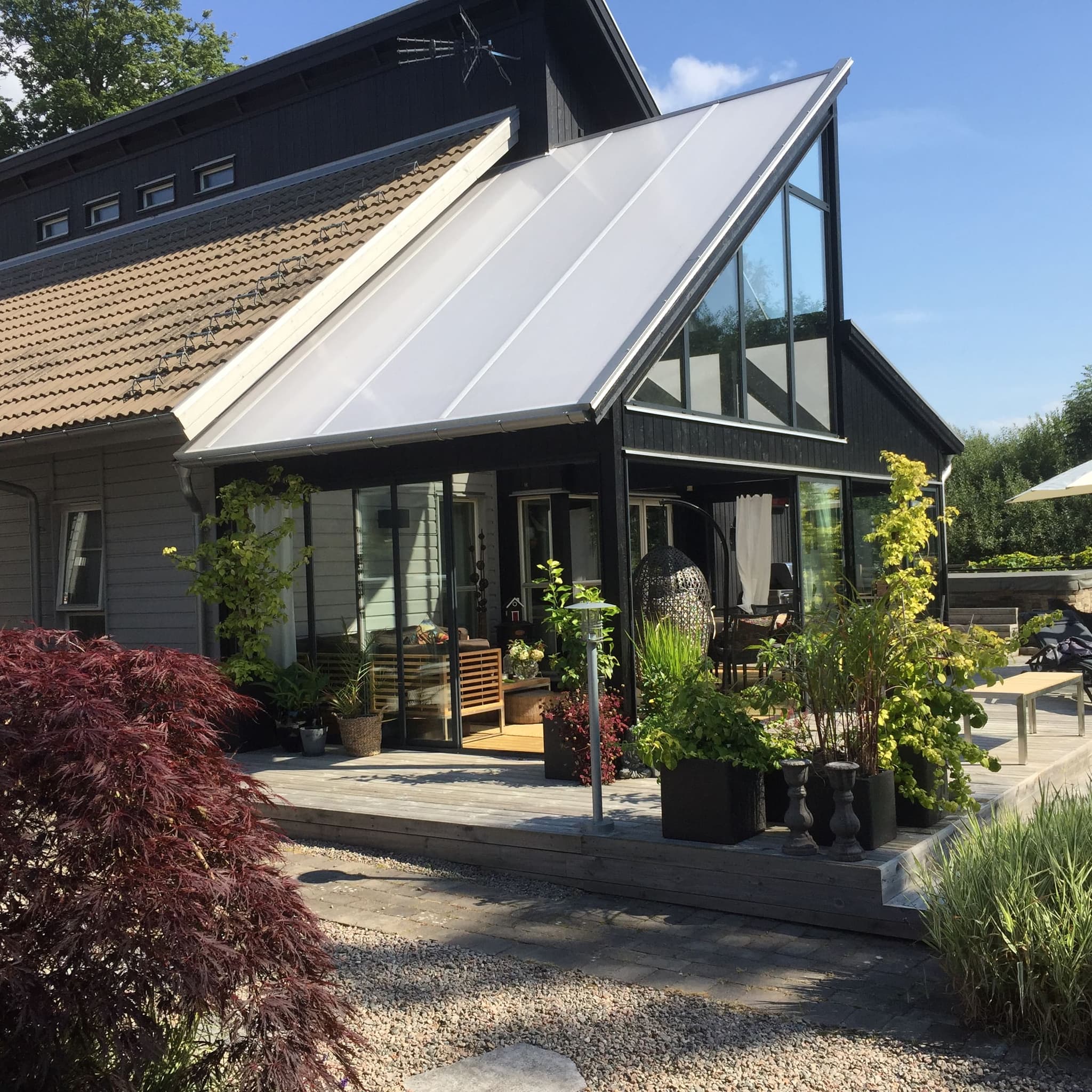 Uterum i glas med svarta ramar anslutet till en villa, med krukväxter på uteplatsen framför