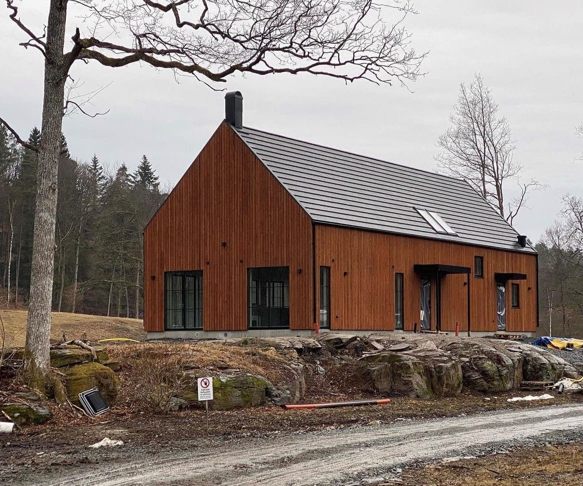 Nybyggd villa med rödbrun stående träpanel och plåttak, uppförd av Enens Bygg